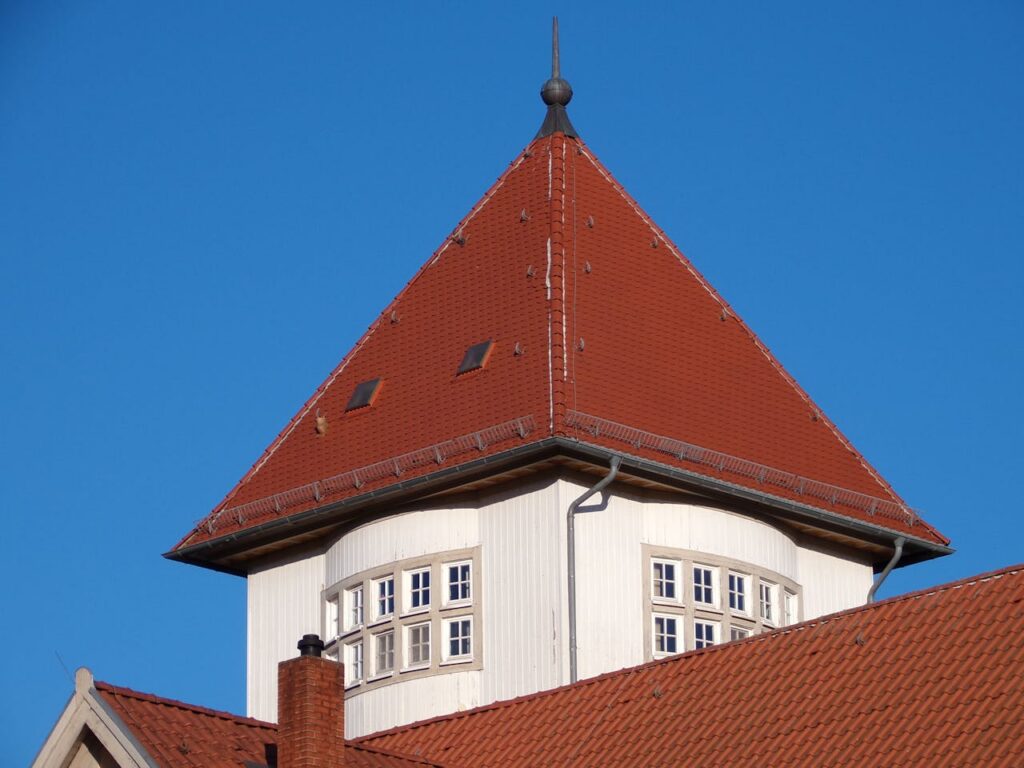 Close-up of a red tiled roof with a triangular peak on a historic building against a clear blue sky.